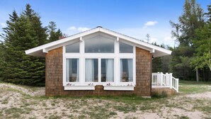 Une petite cabane à un seul étage, dotée d’un toit à pignon, de grandes fenêtres et d’un petit porche avec une balustrade.