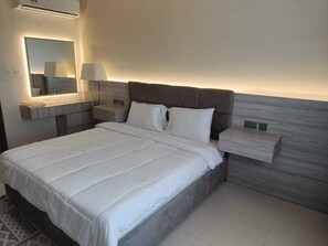 A modern hotel room with a large bed, a bedside table with a lamp, a nightstand, and a wall-mounted mirror. - "Sahwa Residency" our cozy 2-bedroom fully furnished apartments Taqah / Salalah (Taqah)