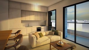 A modern living room with a sofa, coffee table, and wooden chairs. A kitchen area with cabinets and a stove is visible. Large windows offer a view of the city. - Kibaima Apartments (Oranjestad)