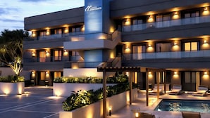 A multi-story hotel with a pool area, outdoor seating, and well-lit balconies. - Kibaima Apartments (Oranjestad)