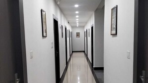 A long, narrow hallway with white walls and black doors, leading to a room at the end. - Hotel Temple View (Gaya)