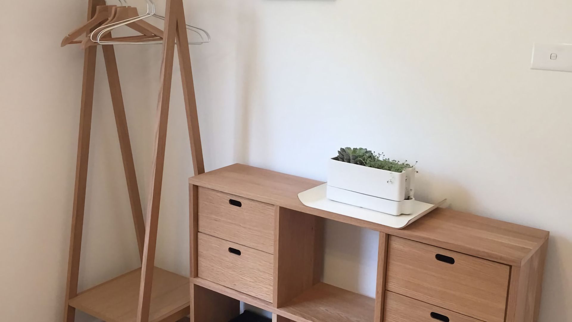Een houten bureau met laden en een plant erop, tegen een effen muur.