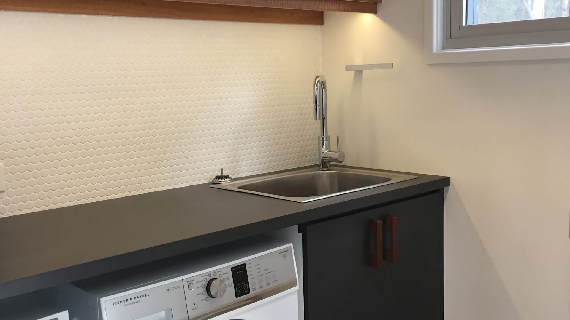 A kitchen with a dishwasher, a stainless steel sink, and a white textured backsplash.