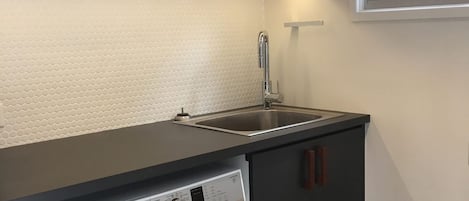 A kitchen with a dishwasher, a stainless steel sink, and a white textured backsplash.