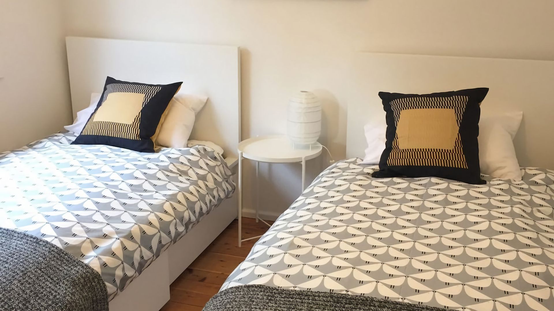Two twin beds with patterned bedding, a small white round table, and a white lamp.