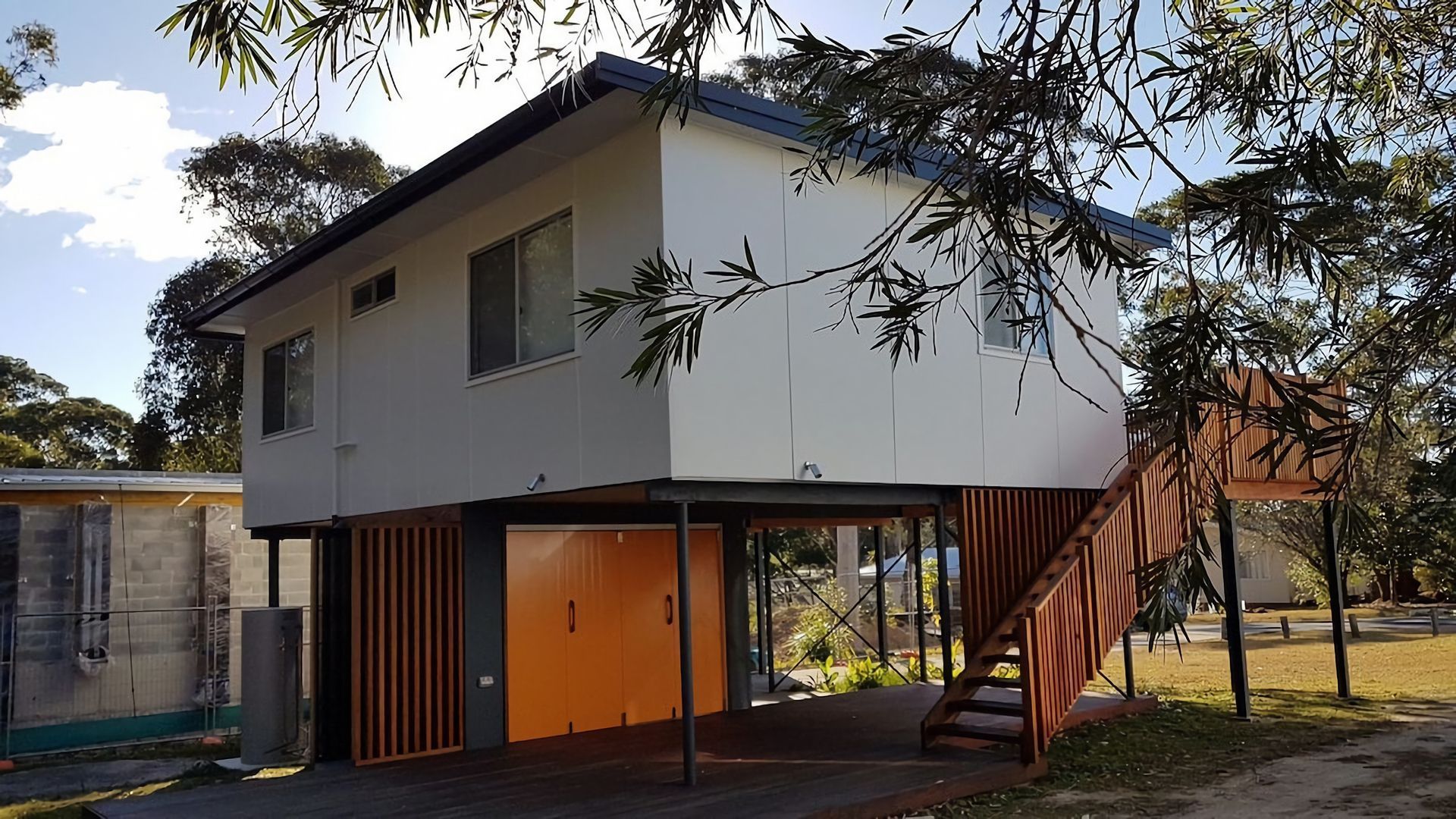 A modern two-story house with a flat roof, a front porch, and a staircase leading to the upper floor.