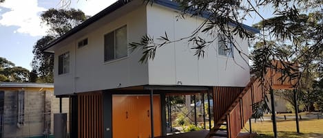 Ein modernes, zweistöckiges Haus mit flachem Dach, einer Veranda und einer Treppe, die zum oberen Stockwerk führt.