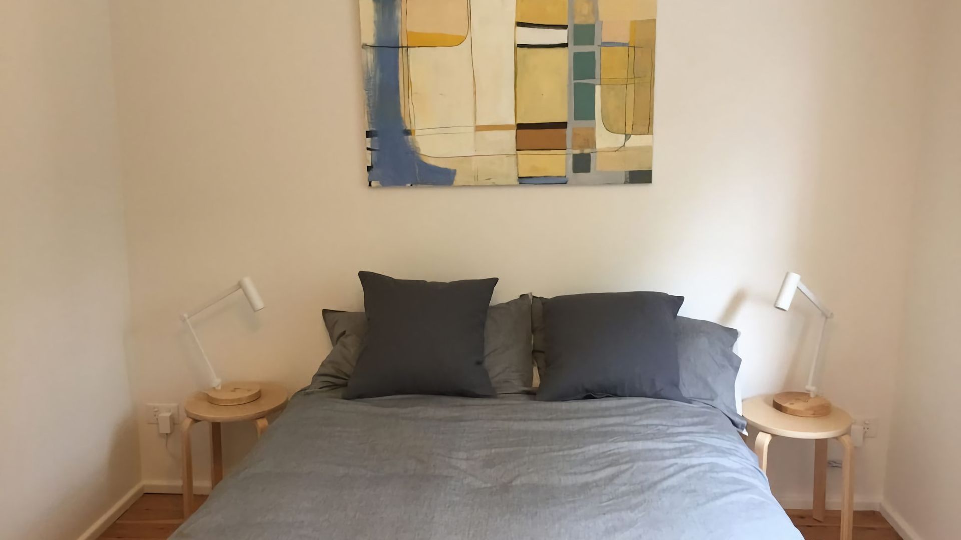 A bedroom with a bed, two bedside tables, and a wall-mounted abstract painting.