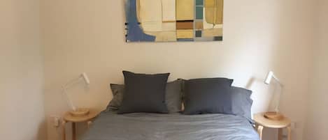 A bedroom with a bed, two bedside tables, and a wall-mounted abstract painting.