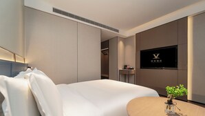 A modern hotel room with a large bed, a small table with a plant, a TV mounted on the wall, and a closet. - Jinglai Hotel Shanghai Songjiang  (Shanghai)