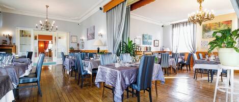 Un'ampia sala da pranzo con pavimento in legno, diversi tavoli apparecchiati e raffinate lampadari.