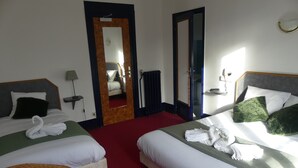 Hotellihuone, jossa on kaksi sänkyä, punainen matto, rottinkituoli, pöytä, jossa on kaukosäädin, ja peili.