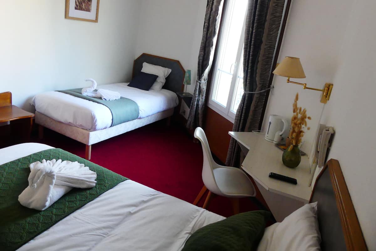 A hotel room with two beds, a desk, a chair, a lamp, and a window with curtains.