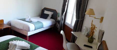 Een hotelkamer met twee bedden, een bureau, een stoel, een lamp en een raam met gordijnen.