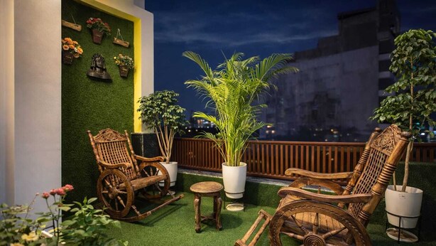 A rooftop terrace with wooden rocking chairs, a small table, and potted plants. - Room Racers (Varanasi)