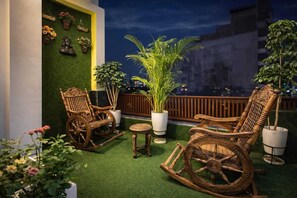 A rooftop terrace with wooden rocking chairs, a small table, and potted plants. - Room Racers (Varanasi)