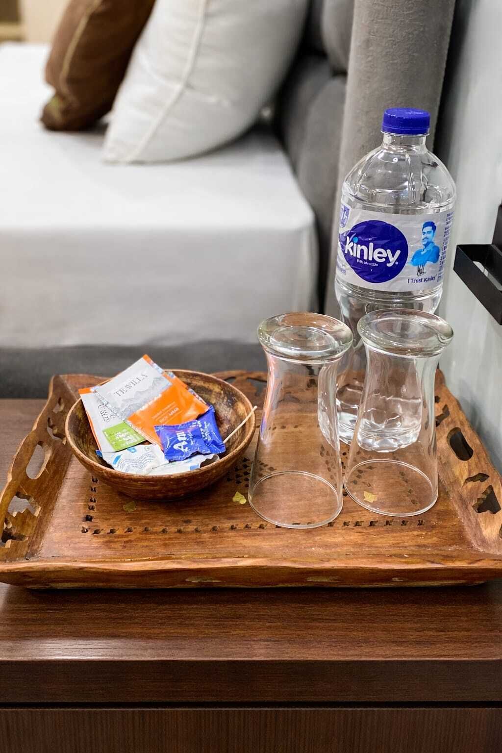 Un plateau en bois sur lequel se trouvent une bouteille d’eau Kinley, un bol de collations et deux verres vides.