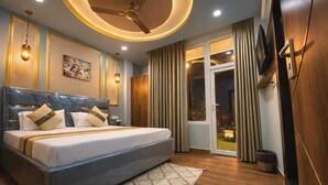 A modern bedroom with a large bed, a ceiling fan, and a view of the outdoors through a sliding glass door. - Room Racers (Varanasi)