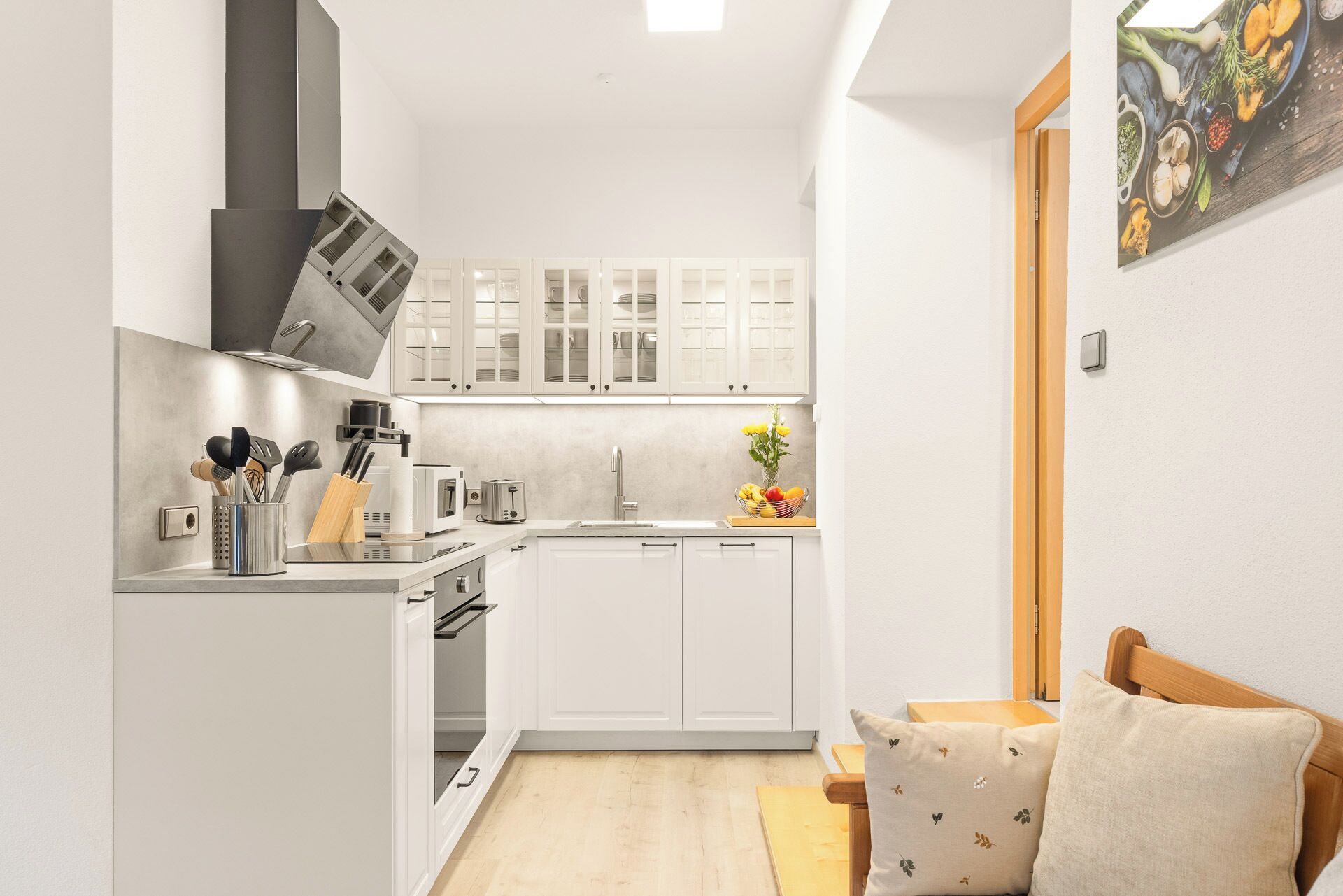 A compact kitchen with white cabinets, a built-in oven, and a sink. There is a small dining area with a wooden table and chairs.