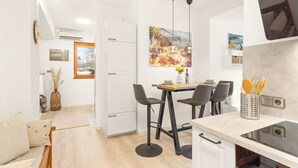 Uma cozinha compacta com área de jantar, apresentando uma geladeira branca, uma mesa de jantar com quatro cadeiras e uma pintura sobre a mesa.