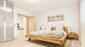 Quarto com cama de madeira, mesa de cabeceira, luminária na parede e um quadro sobre a cama.