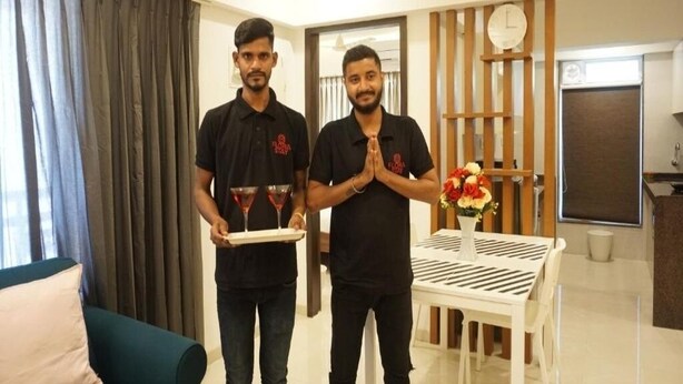 Two individuals in black shirts holding a tray with two drinks and a vase with flowers. - 2BR Service Apartment 301 Chembur by FLORA STAYS (Mumbai)