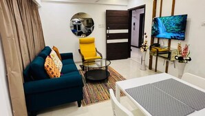 A living room with a sofa, a yellow armchair, a glass coffee table, a TV, and a mirror. - 2BR Service Apartment 301 Chembur by FLORA STAYS (Mumbai)
