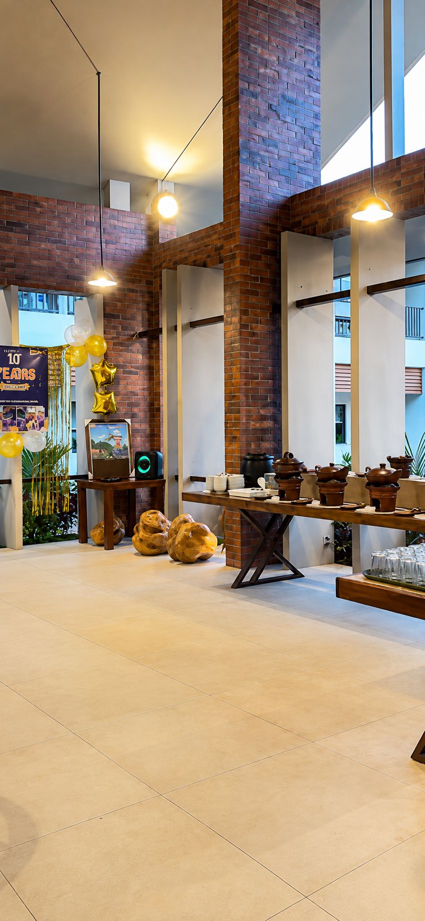 A spacious room with exposed brick walls, a long table with teapots and cups, and a banner indicating a celebration.