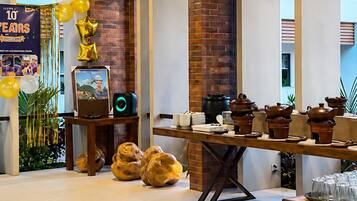 A spacious room with exposed brick walls, a long table with teapots and cups, and a banner indicating a celebration.