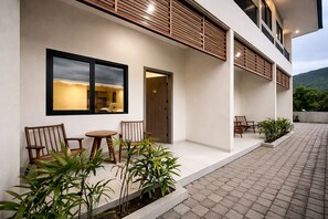 Ein modernes Geb äude mit flachem Dach, einem Balkon mit Holzgeländern und einer gepflasterten Außenfläche mit Sitzgelegenheiten.
