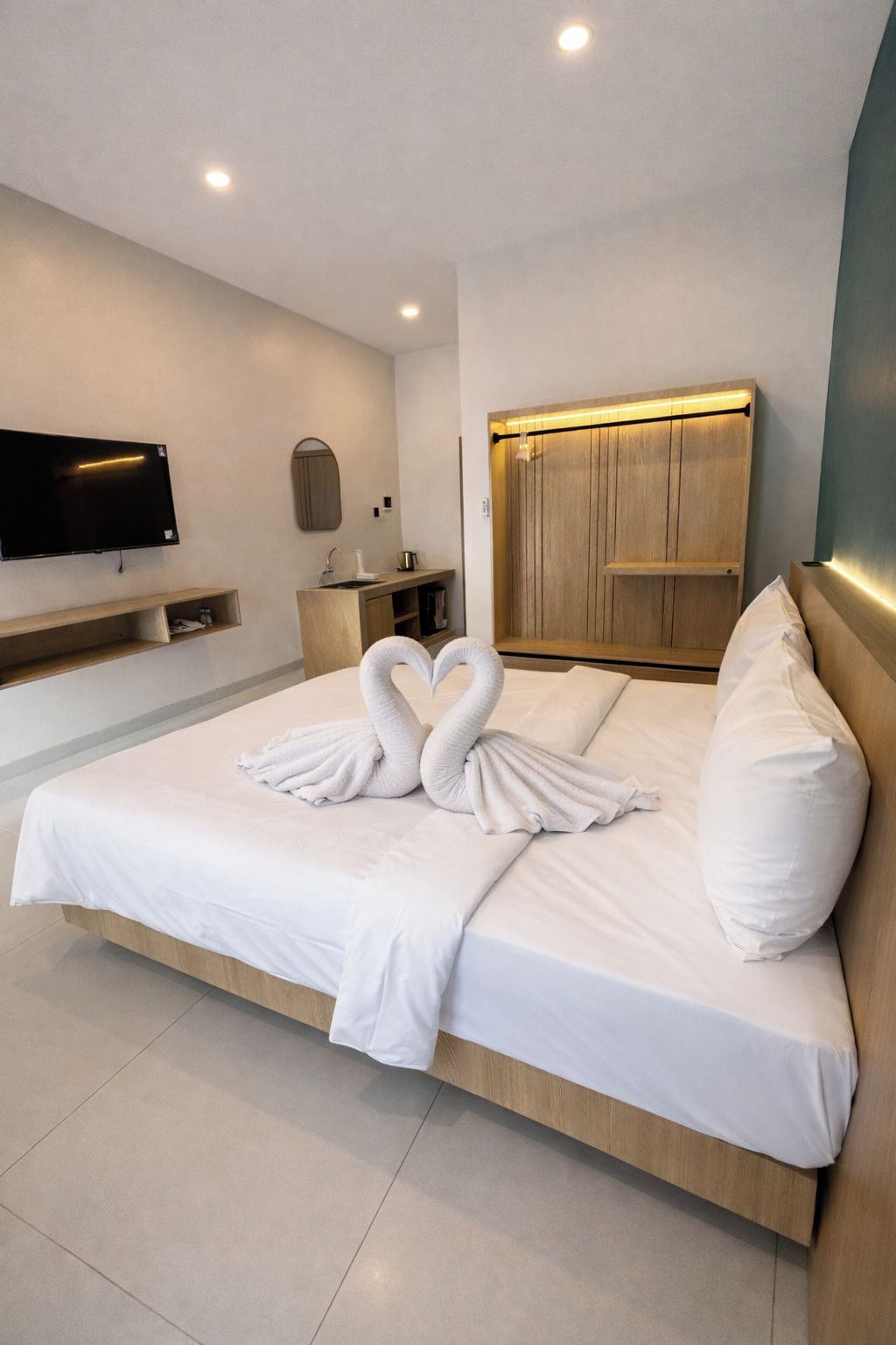 Habitación de hotel con una cama grande, un televisor montado en la pared, un cabecero de madera y un armario de madera.