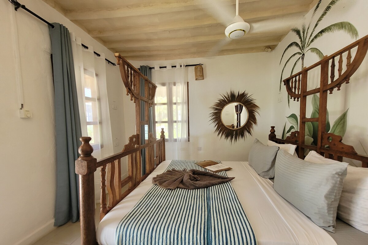 A bedroom with a wooden bed frame, a round mirror, and a view of palm trees through the window.
