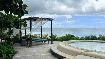 A pool area with a pergola, lounge chairs, and a view of the ocean.