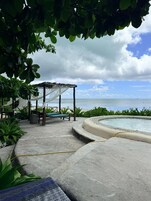 A pool area with a pergola, lounge chairs, and a view of the ocean.