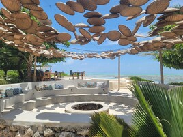 Un espace aménagé près de la plage, avec un foyer circulaire en pierre, du mobilier d’extérieur et une vue sur l’océan.