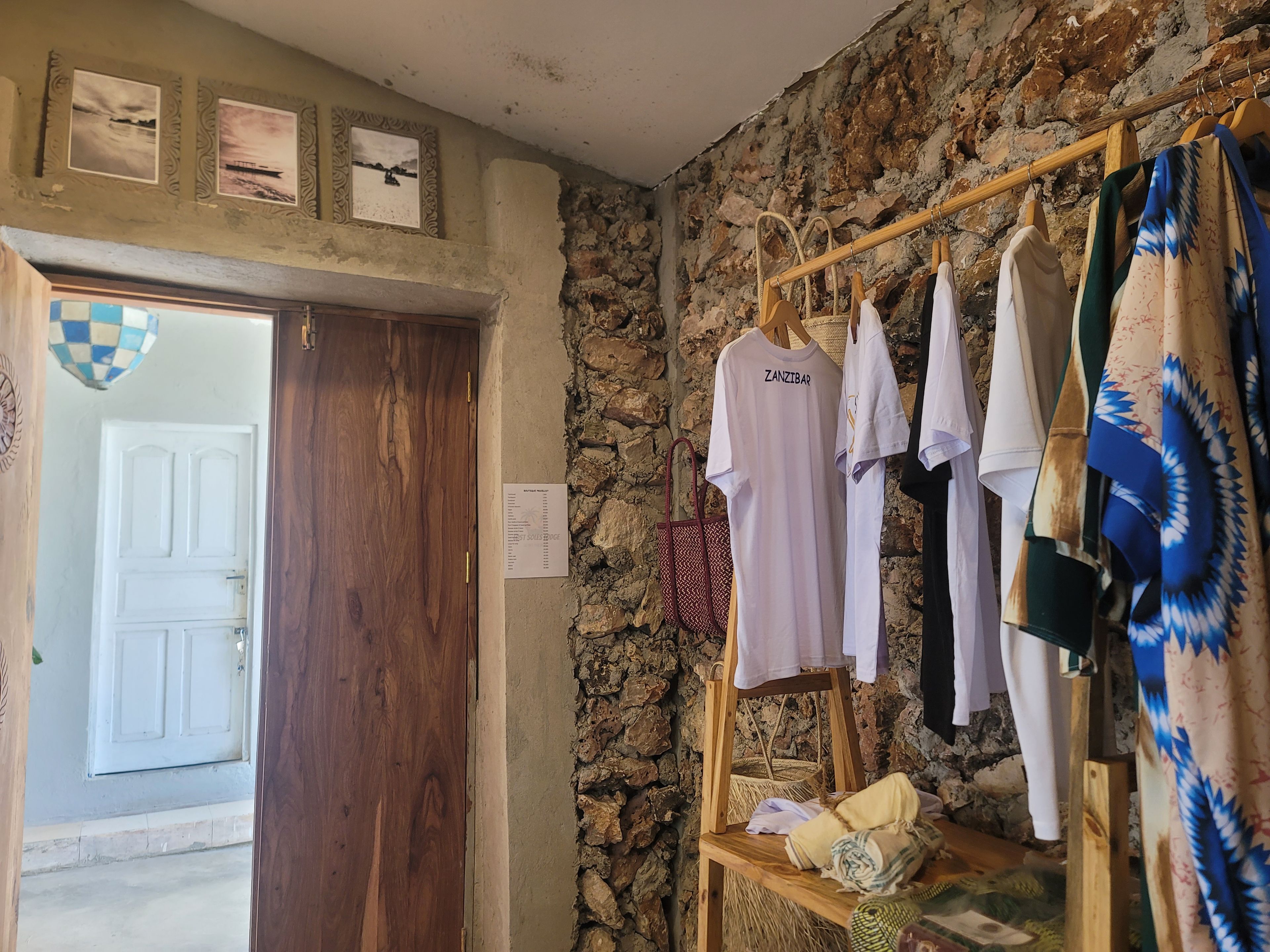 A room with a wooden door, a stone wall, and a clothing rack with various garments.