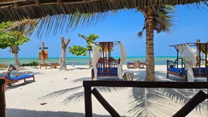 Ein Strand mit strohgedeckten Gebäuden, Holzbänken und freiem Blick auf das Meer.
