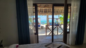 A room with a bed, a view of a beach, and a thatched-roof structure. - Lost Soles Lodge (Jambiani)