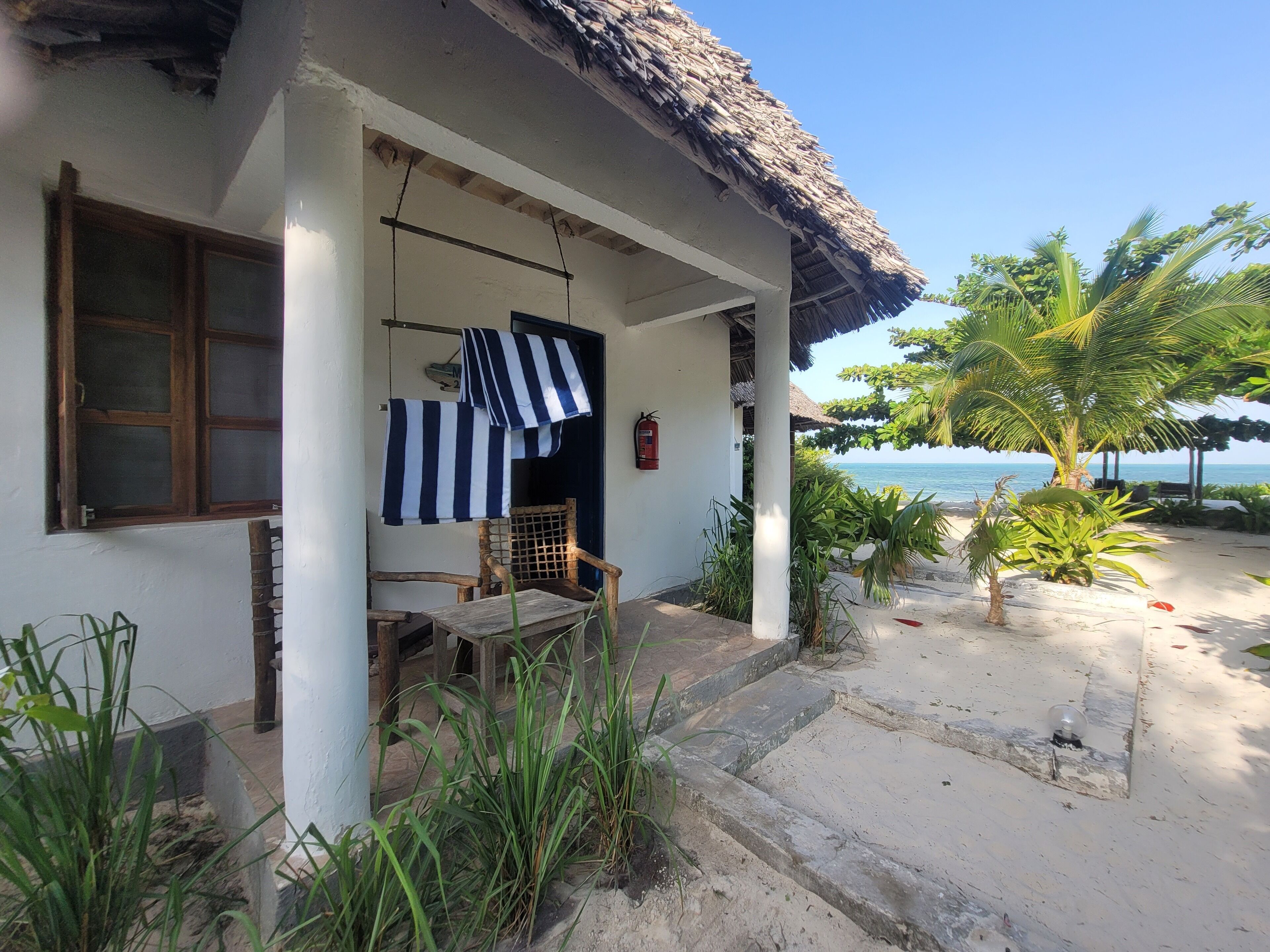 Une maison de plage avec un toit de chaume, une chaise en bois et une vue sur l’océan.