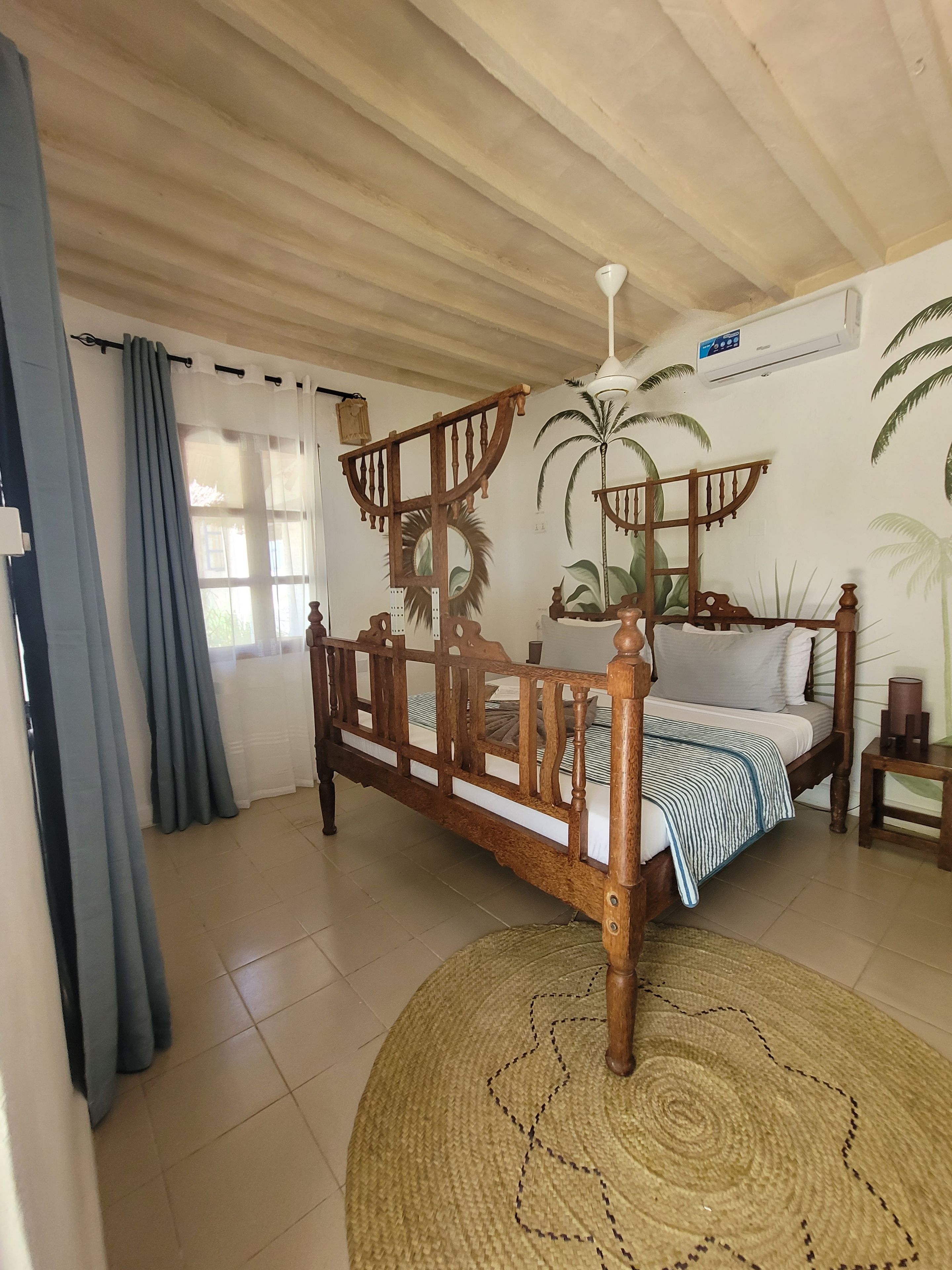 A room with a wooden bed, a ceiling fan, and a wall with palm tree murals.