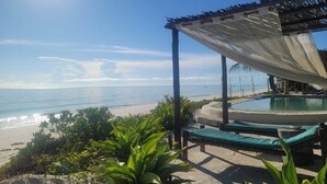 A beachside pool area with lounge chairs and a pergola providing shade. - Lost Soles Lodge (Jambiani)