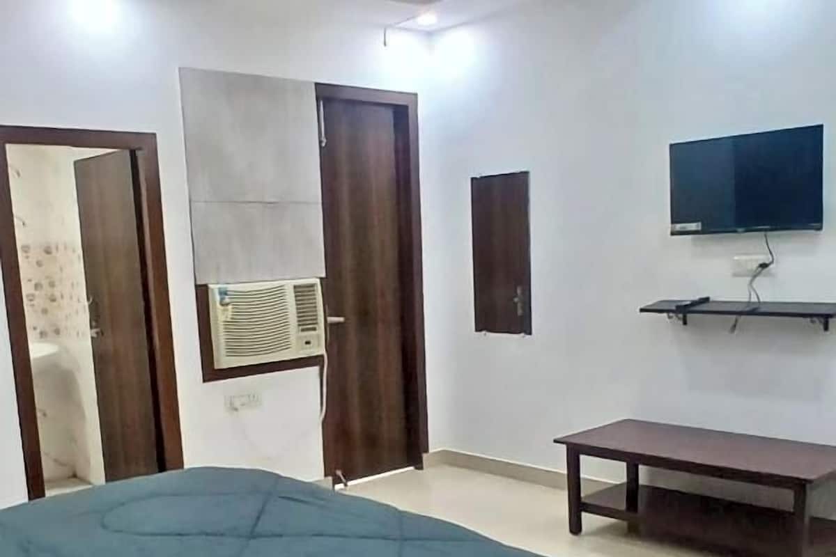A bedroom with a bed, a ceiling fan, a TV mounted on the wall, and a small table.