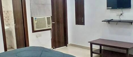 A bedroom with a bed, a ceiling fan, a TV mounted on the wall, and a small table.