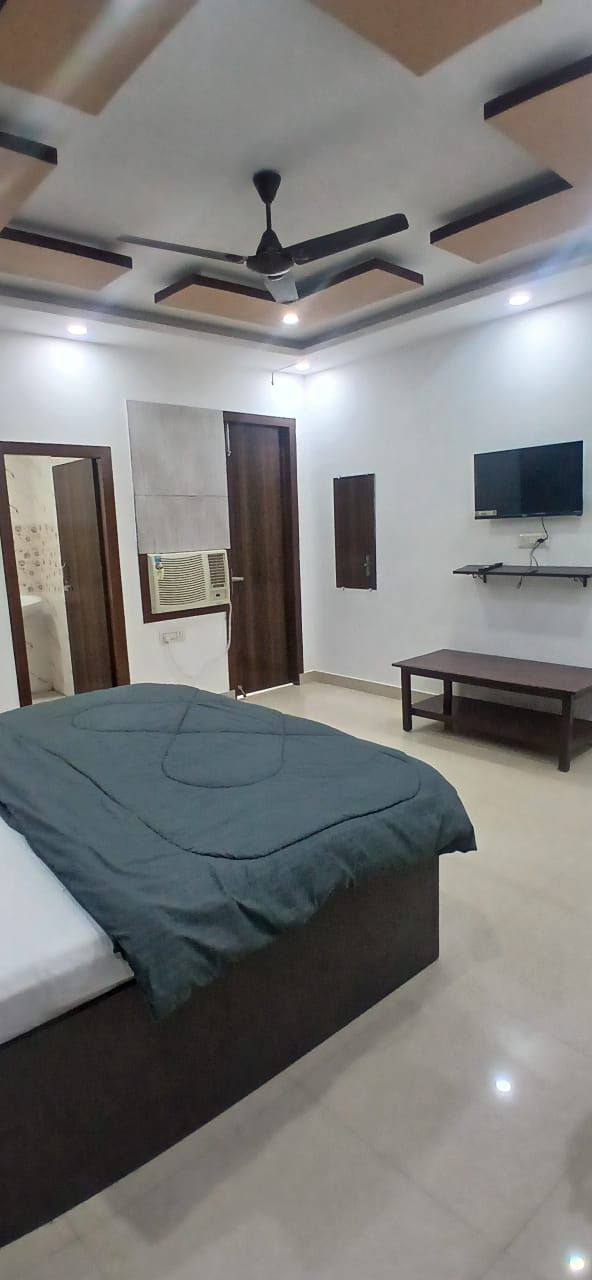 A bedroom with a bed, a ceiling fan, a TV, and a window.
