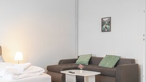 A modern hotel room with a brown sofa, a small white table, a lamp, and a framed picture on the wall. - Cozy 2BR Stay Near AKH With WiFi (Vienna)