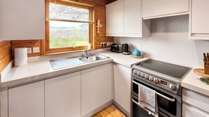 Een kleine keuken met een spoelbak, fornuis en een raam met uitzicht op een groen landschap.