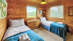 Een houten kamer met twee bedden, een dressoir en grote ramen.
