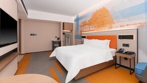 Ett hotellrum med en säng, ett nattduksbord med en telefon, en TV och ett konstverk som hänger på väggen.