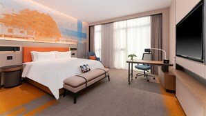 Una habitación de hotel con una cama grande, un escritorio, un televisor y una ventana con cortinas.