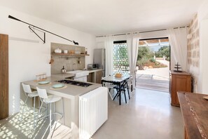 Een moderne keuken met een centraal eiland, witte barkrukken en een eettafel met stoelen.